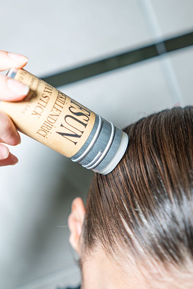 Person applying a hair product labeled 'NOSH' to their hair.